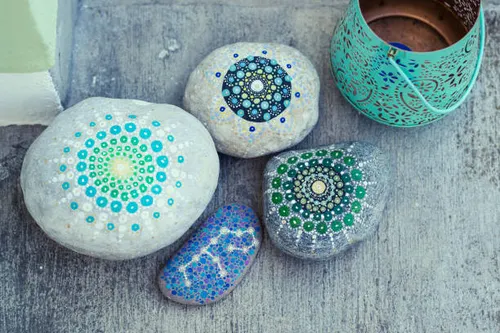Hand-painted mandala stones in blues and greens beside a tealight lantern